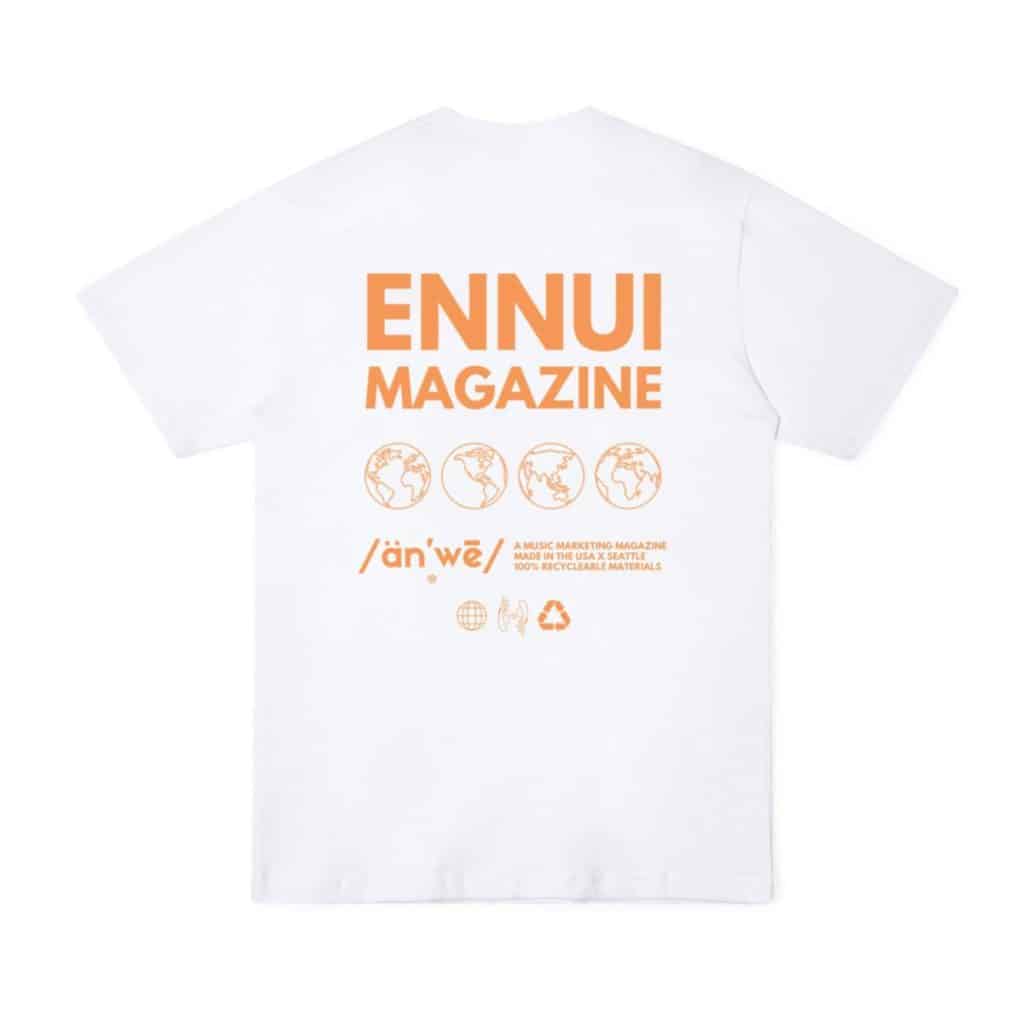 A white T-shirt with bold orange branding on the back. It prominently features the text "ENNUI MAGAZINE" in large font, along with globe icons and eco-friendly icons indicating it is made in the USA from 100% recyclable materials. The bottom section includes the phonetic pronunciation "/än'we/" and sustainability symbols.