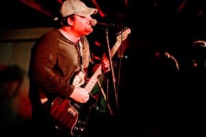 A guitarist playing energetically under dim, moody lighting, highlighting the motion and intensity of the performance.