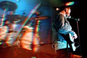 A musician from The National Parks performing on stage with a guitar, captured in a vibrant double-exposure image that showcases movement and colorful light effects.