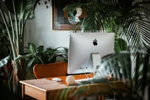 An Apple computer on a desk surrounded by plants