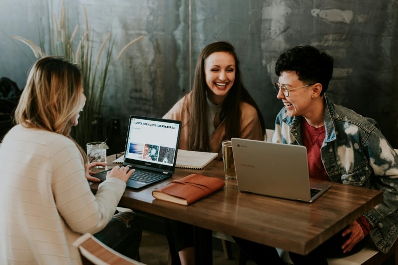 Three people using laptops and smiling